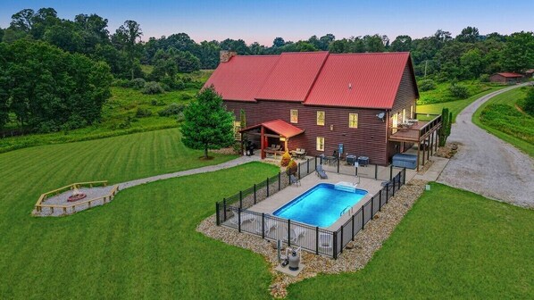 A large house with a red roof, a swimming pool, and a well-maintained lawn.