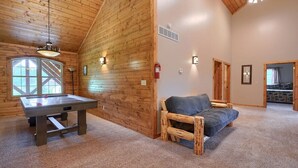 Ein gemütliches Zimmer mit Holzwänden, einem Billardtisch, einer Couch und einem Kamin.