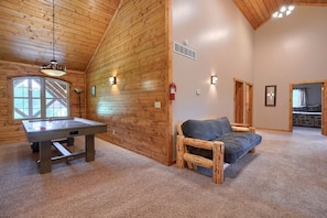 A cozy room with wooden walls, a pool table, a sofa, and a fireplace.