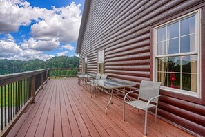 A wooden cabin with a deck, a table with chairs, and a large window.