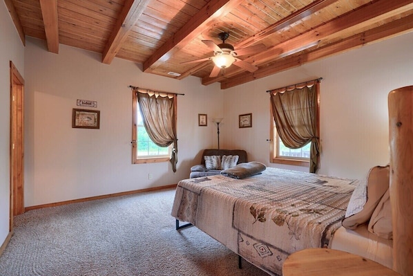 A bedroom with a bed, a chair, a ceiling fan, and two windows with curtains.