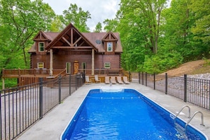 A wooden cabin with a swimming pool, surrounded by a deck and a fence.