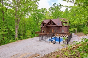 A rustic cabin with a wooden exterior, a deck, and a pool area surrounded by a fence.