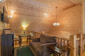 A cozy cabin interior with a wooden ceiling, a sofa, a table, and a lamp. - Grand Bentley | Hocking Hills, Pool & Theater (Rockbridge)