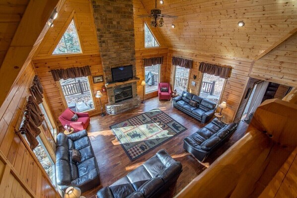 A cozy cabin interior with a fireplace, leather sofas, and a large window overlooking a deck.