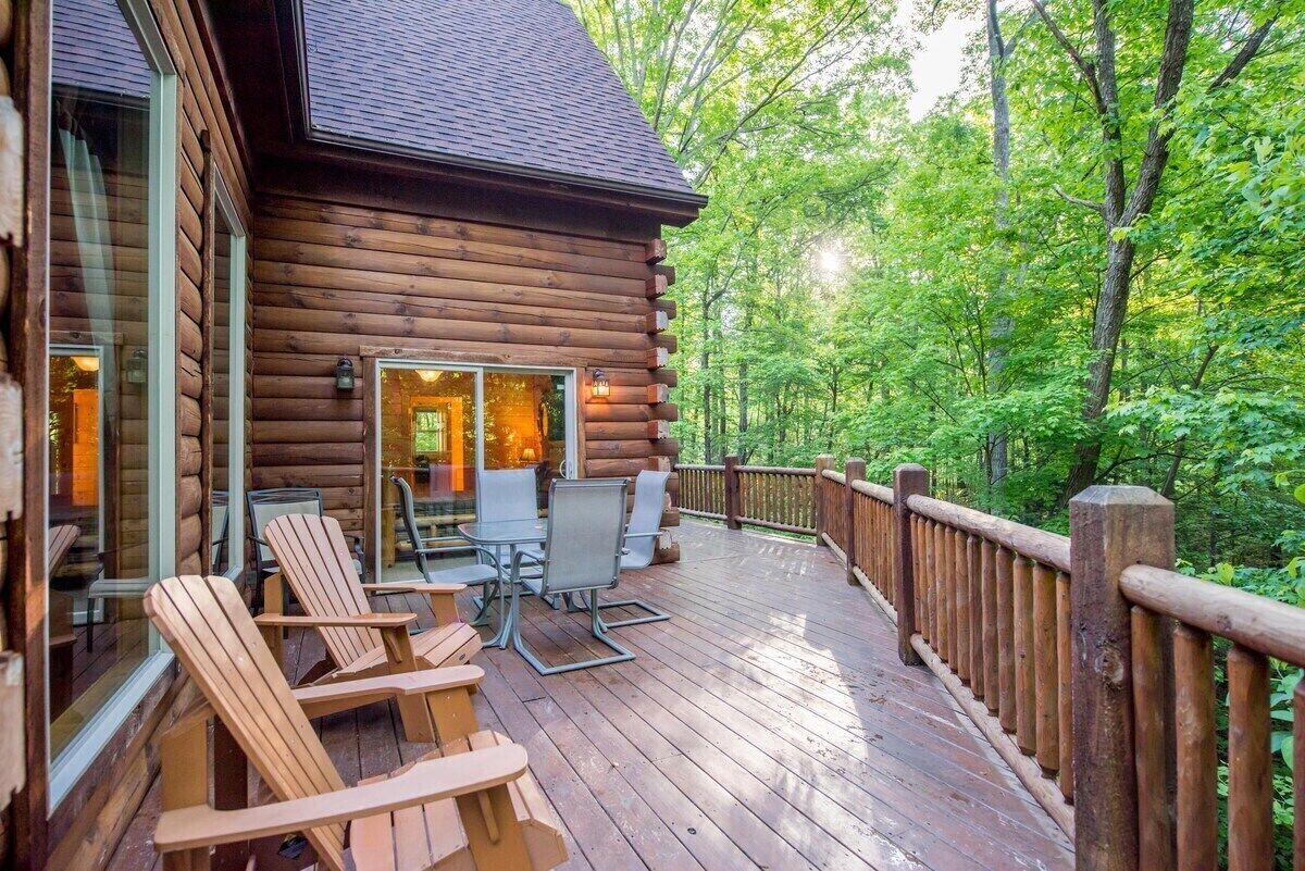 A log cabin with a deck, outdoor seating, and a forested backdrop.