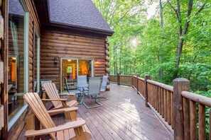 A log cabin with a deck, outdoor seating, and a forested backdrop. - Grand Bentley | Hocking Hills, Pool & Theater (Rockbridge)