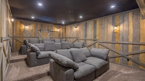 A cozy home theater with a sectional sofa, wooden walls, and ceiling lights. - Grand Bentley | Hocking Hills, Pool & Theater (Rockbridge)