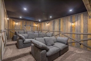 Un salon cinéma chaleureux, avec un canapé d’angle, des murs en bois et des luminaires au plafond.