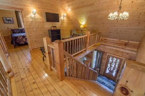 L’intérieur d’une cabane en bois, avec une chambre à coucher située en mezzanine, un escalier et un lustre.