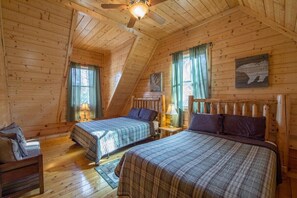 A log cabin bedroom with two beds, wooden walls, a sloped ceiling, and a ceiling fan. - Grand Bentley | Hocking Hills, Pool & Theater (Rockbridge)