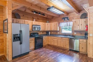 A wooden cabin-style kitchen with a refrigerator, stove, microwave, and dishwasher. - Grand Bentley | Hocking Hills, Pool & Theater (Rockbridge)