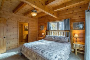 A wooden cabin bedroom with a bed, two bedside tables, a window with curtains, and a ceiling light.