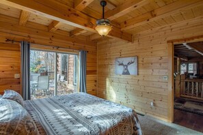 A log cabin bedroom with a bed, a ceiling fan, a large window, and a deer painting on the wall.