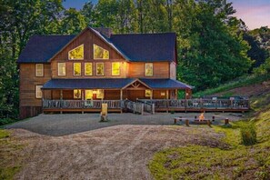 Eine große Holzhütte mit einer Veranda und einem Feuerstellenbereich.