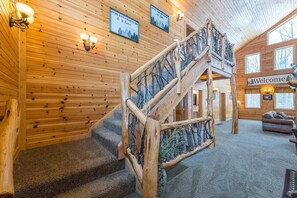 A wooden interior with a staircase, a 'Welcome' sign, and framed pictures on the walls. - Creek Lodge | Hocking Hills, 7BR, Pool, Theater (Rockbridge)