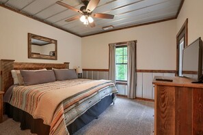 A bedroom with a wooden headboard, a large bed with a striped blanket, a ceiling fan, a window with curtains, and a wooden dresser.