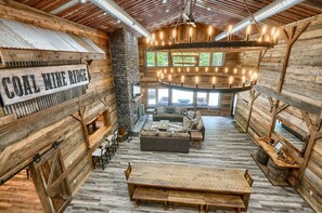 A rustic interior with a sign reading 'COAL MINE RIDGE,' wooden walls, a stone pillar, a round wooden table, a sofa, and a hanging light fixture. - Coal Mine | Hocking Hills, 8BR, Pool & Bowling (Logan)