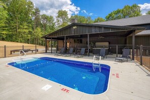 A swimming pool with a covered patio area, lounge chairs, and a building with a metal roof.