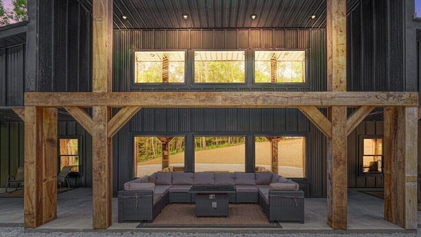 A modern outdoor seating area with a sectional sofa and a coffee table, framed by wooden beams and large windows. - Coal Mine | Hocking Hills, 8BR, Pool & Bowling (Logan)