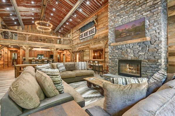 A spacious interior with a stone fireplace, a dining area, and a high ceiling with exposed beams.