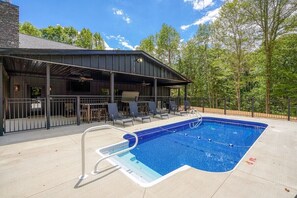 A pool area with a covered seating area and a pool with a ladder.
