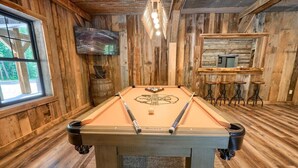 A pool table in a room with wooden walls and a bar area. - Coal Mine | Hocking Hills, 8BR, Pool & Bowling (Logan)