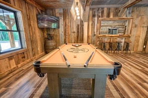 A pool table in a room with wooden walls and a bar area. - Coal Mine | Hocking Hills, 8BR, Pool & Bowling (Logan)