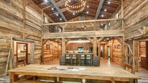 A rustic wooden interior with a central dining table, a kitchen area, and a mezzanine level. - Coal Mine | Hocking Hills, 8BR, Pool & Bowling (Logan)