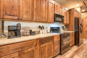 Una cocina con armarios de madera, microondas, cafetera y refrigerador.