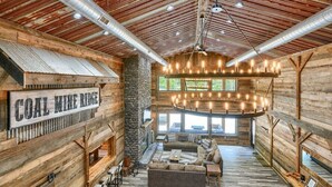 A rustic interior with a stone fireplace, wooden walls, and a large chandelier. - Coal Mine | Hocking Hills, 8BR, Pool & Bowling (Logan)