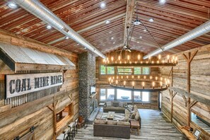A rustic interior with a stone fireplace, wooden walls, and a large chandelier. - Coal Mine | Hocking Hills, 8BR, Pool & Bowling (Logan)