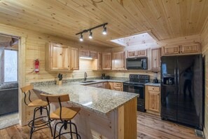 L’intérieur d’un chalet en bois comprend une cuisine dotée de plans de travail en granit, de meubles en bois, d’un réfrigérateur noir et d’un coin bar avec des tabourets.