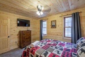 Une chambre dans un chalet en bois, comprenant un lit, une commode, un téléviseur et un ventilateur de plafond.