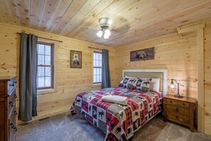 A wooden cabin bedroom with a bed, two windows, a ceiling fan, and a nightstand. - Hideaway Cabin | Hocking Hills, 7 Private Acres (Logan)