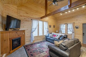A log cabin interior with a fireplace, a television, a sofa, and a patterned rug.