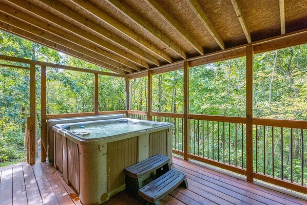 A hot tub on a wooden deck with a view of a forest.
