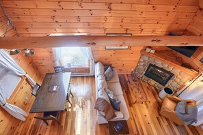 Interior acogedor de una cabaña con chimenea de piedra, pisos de madera, un sofá, una mesa de comedor y una pequeña zona de estar.