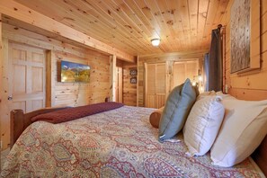 A wooden cabin bedroom with a bed, pillows, a blanket, and a painting on the wall. - Tranquility Ridge | Hocking Hills, 5 Acres, Pets (Logan)