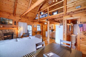 Interior d'una cabana amb una llar de pedra, un sofà, una taula de dinar i una zona de cuina.