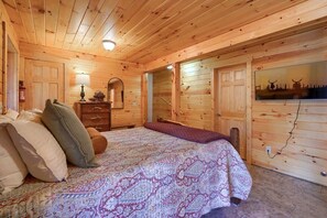 Un dormitorio de cabaña de madera con cama, almohadas, cómoda, espejo y televisor de pared.
