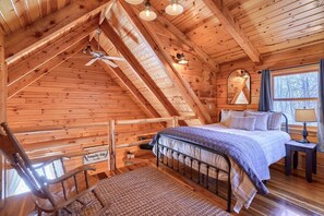 A cozy cabin bedroom with a wooden ceiling, a bed, a chair, a nightstand, and a window.