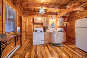 A cabin-style kitchen with wooden walls, a white stove, a microwave, and a refrigerator. - Tranquility Ridge | Hocking Hills, 5 Acres, Pets (Logan)