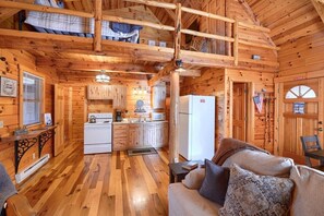 A cabin interior with a kitchen, dining area, and a loft bedroom.