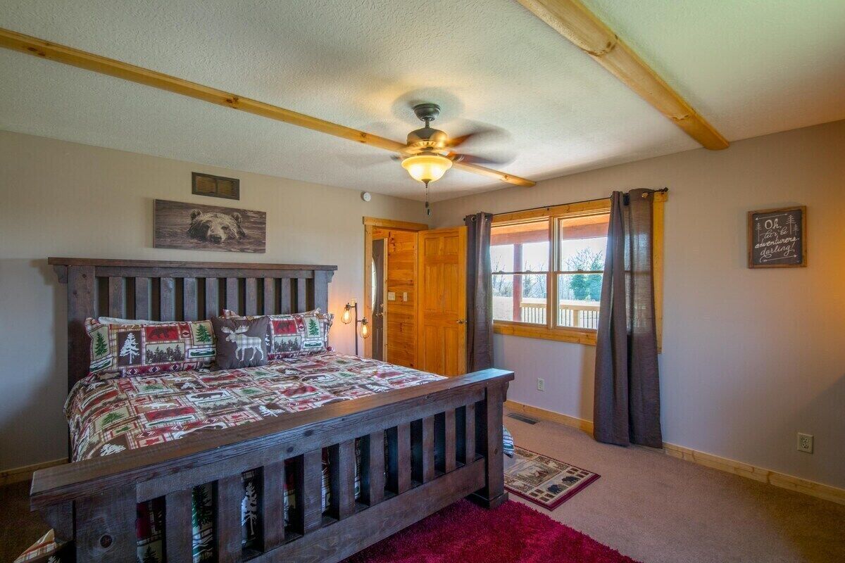 A bedroom with a wooden bed, a ceiling fan, a window with curtains, and a door.