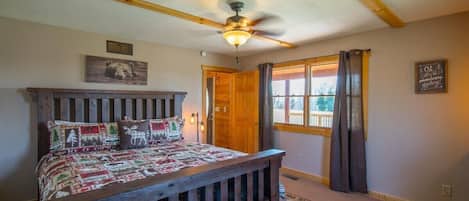 A bedroom with a wooden bed, a ceiling fan, a window with curtains, and a door.