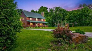 A rustic log cabin with a green roof, surrounded by lush greenery and a well-maintained lawn.
