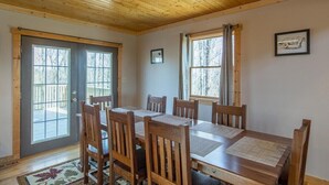 A dining room with a wooden table and chairs, large windows, and a ceiling fan.