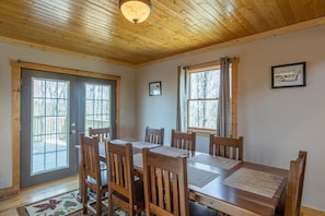 A dining room with a wooden table and chairs, large windows, and a ceiling fan. - Dragonfly Lodge | Hocking Hills, 5BR, Hot Tub (Logan)