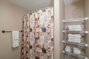 Un baño con cortina de ducha con estampado de motivos naturales, un perchero con toallas dobladas y un estante con toallas ordenadas.